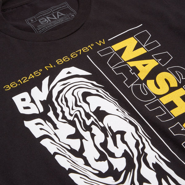 Detail shot of the Saturday Graphic T-Shirt.  Black t-shirt with full front graphic design featuring the BNA latitude and longitude coordinates, a swirled BNA design, and Nashville printed vertically in solid yellow with a white outline.  A small yellow plane travels across the bottom of the design to finish the frame.